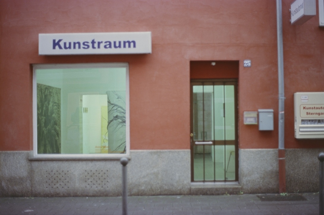 Eksteriør af et kunstgalleri ved navn 'Kunstraum', som viser en typisk facade for en gallerivirksomhed med et stort vindue.